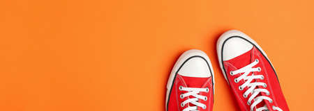 Pair of red sneakers on orange background, space for text