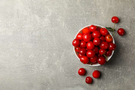 Bowl with red cherry on gray background, top view