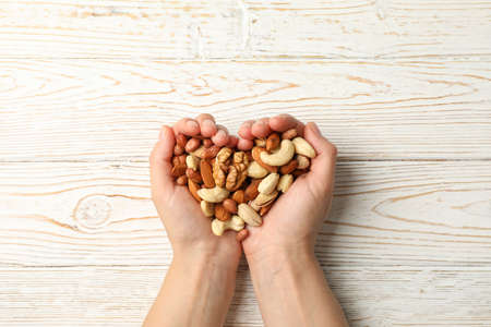 Woman holds different nuts on wooden background. Healthy eatingの写真素材