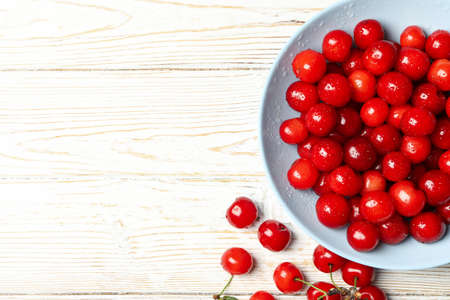 Plate with red cherry on white wooden background, top viewの写真素材