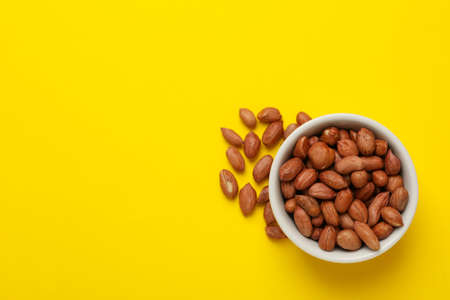 Bowl with peanut on yellow background. Vitamin food