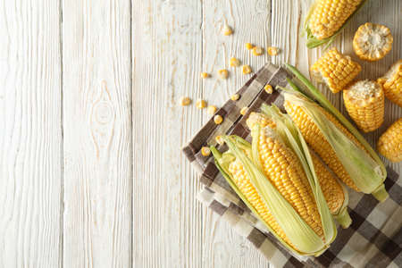 Fresh raw corn and napkin on white wooden background, top view