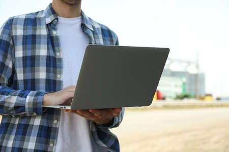 Young man with laptop against grain silos. Agricultureure business