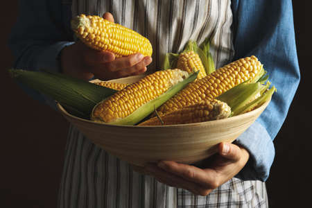 Woman with bowl of fresh corn against brown background