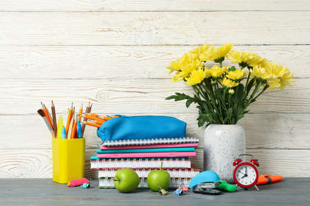 School supplies and flowers in vase on wooden background, space for text