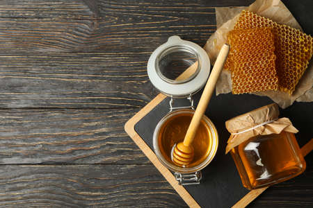 Composition with honeycombs, honey, jars and dipper on wooden background
