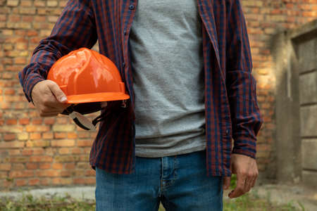 Builder in shirt and jeans holds safety helmet outdoorの写真素材