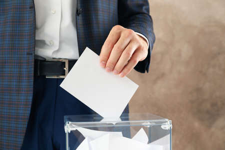 Man putting ballot into voting box on blue background