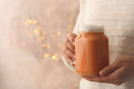 Woman hold glass jar of pumpkin latte against brown background with blurred lightsの写真素材