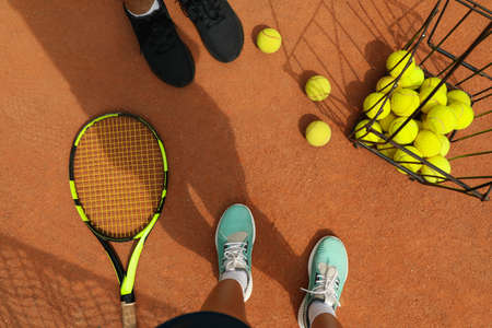 Woman and man legs in sneakers on clay court with tennis balls and racket
