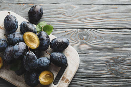 White board with fresh plums on wooden background