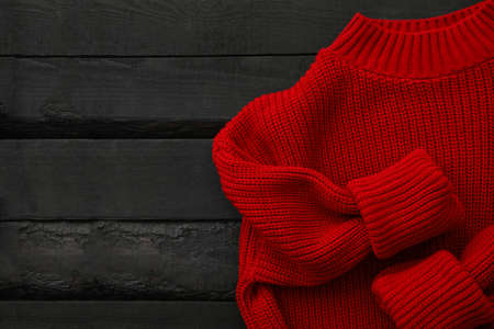 Red knitted sweater on wooden background, top view
