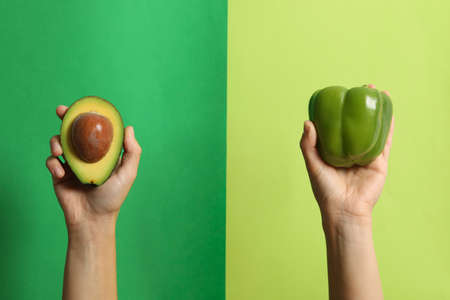 Female hands hold pepper and avocado on two tone backgroundの写真素材
