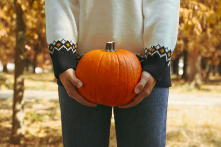 Woman in sweater and jeans hold pumpkin outdoorの写真素材