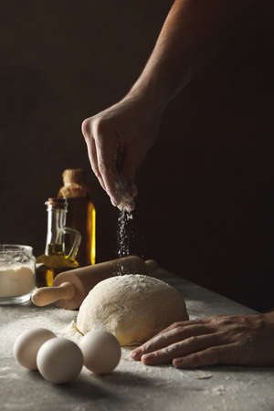 Man sprinkle flour on dough against dark backgroundの写真素材