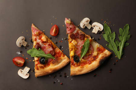 Pizza slices and ingredients on dark background