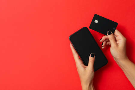 Female hands hold phone and card on red background
