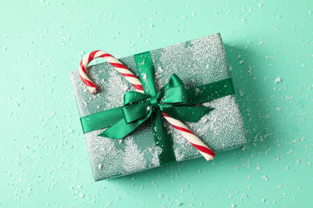Christmas box with candy cane on mint background with snowの写真素材