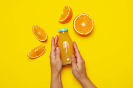 Female hands hold bottle of orange juice on yellow backgroundの写真素材
