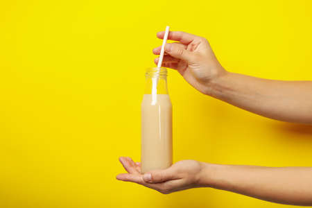 Female hands hold banana juice on yellow backgroundの写真素材