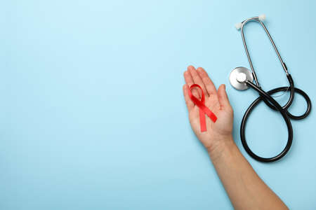 Female hand hold red awareness ribbon on blue background with stethoscopeの写真素材