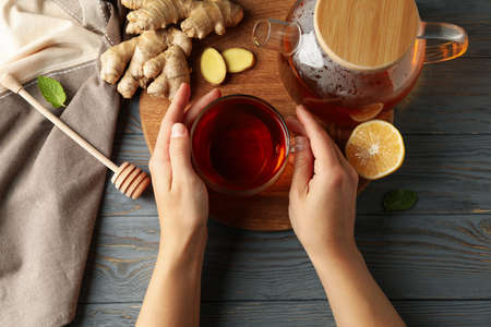 Female hands hold cup of ginger tea on wooden backgroundの写真素材