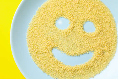 Smile made of couscous in plate on yellow background