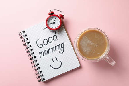 Notebook with text Good morning, clock and cup of coffee on pink backgroundの写真素材