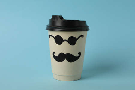 Paper cup with painted mustaches and glasses on blue backgroundの写真素材