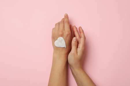 Female hands with heart made of cosmetic cream on pink backgroundの写真素材