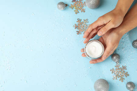 Female hands hold cosmetic cream on blue background with baubles