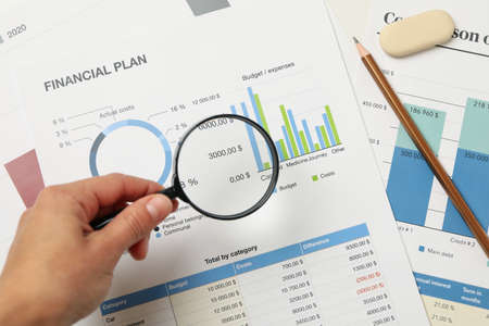 Female hand holding magnifier on financial documents background