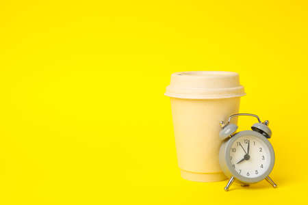 Paper cup and alarm clock on yellow background