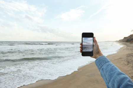Female hand hold phone with making selfie on seaの写真素材