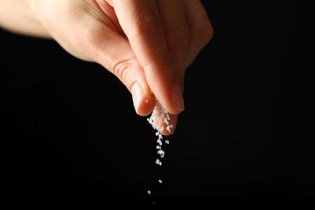 Female hand adding salt on black backgroundの写真素材