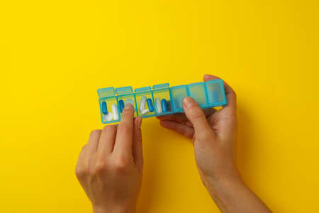 Female hands hold container with pills on yellow background