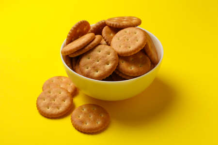 Wooden bowl with tasty cracker biscuits on yellow background