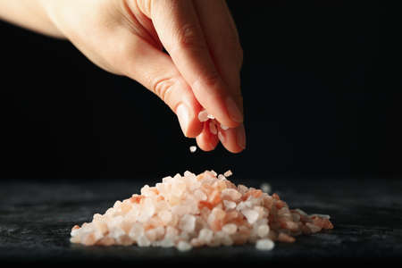 Female hand hold pink himalayan salt on black background, close upの写真素材