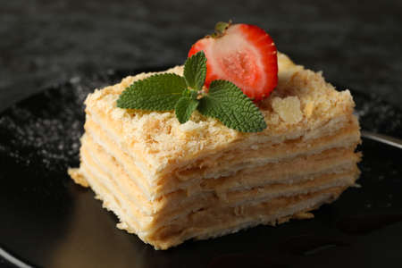 Plate with piece of Napoleon cake with strawberry on black smokey background