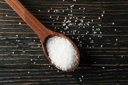 Wooden spoon with salt on wooden background, close up