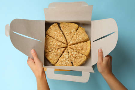 Female hands hold delivery box with Napoleon cake on blue backgroundの写真素材