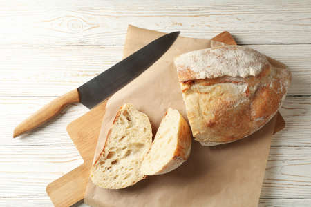 Baking paper with bread and knife on white wooden background