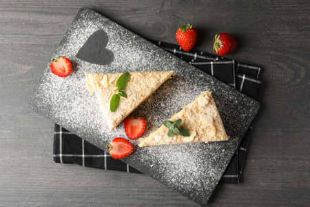 Board with pieces of Napoleon cake with strawberry on black background