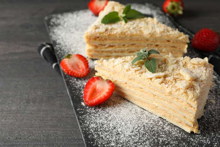 Board with pieces of Napoleon cake with strawberry on black background