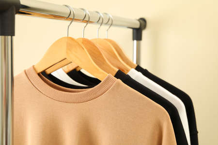 Hangers with stylish sweatshirts on beige backgroundの写真素材