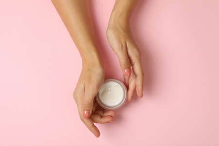 Cute female hands hold jar of cosmetic cream on pink backgroundの写真素材