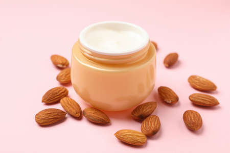 Jar of cosmetic cream and almond on pink backgroundの写真素材
