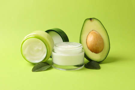 Jars of cosmetic cream, leaves and avocado on green backgroundの写真素材
