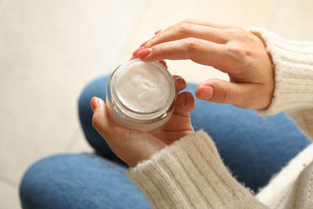 Woman in sweater and jeans hold jar of cosmetic creamの写真素材