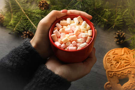 Woman hold cup of drink with marshmallow on black background with cookie